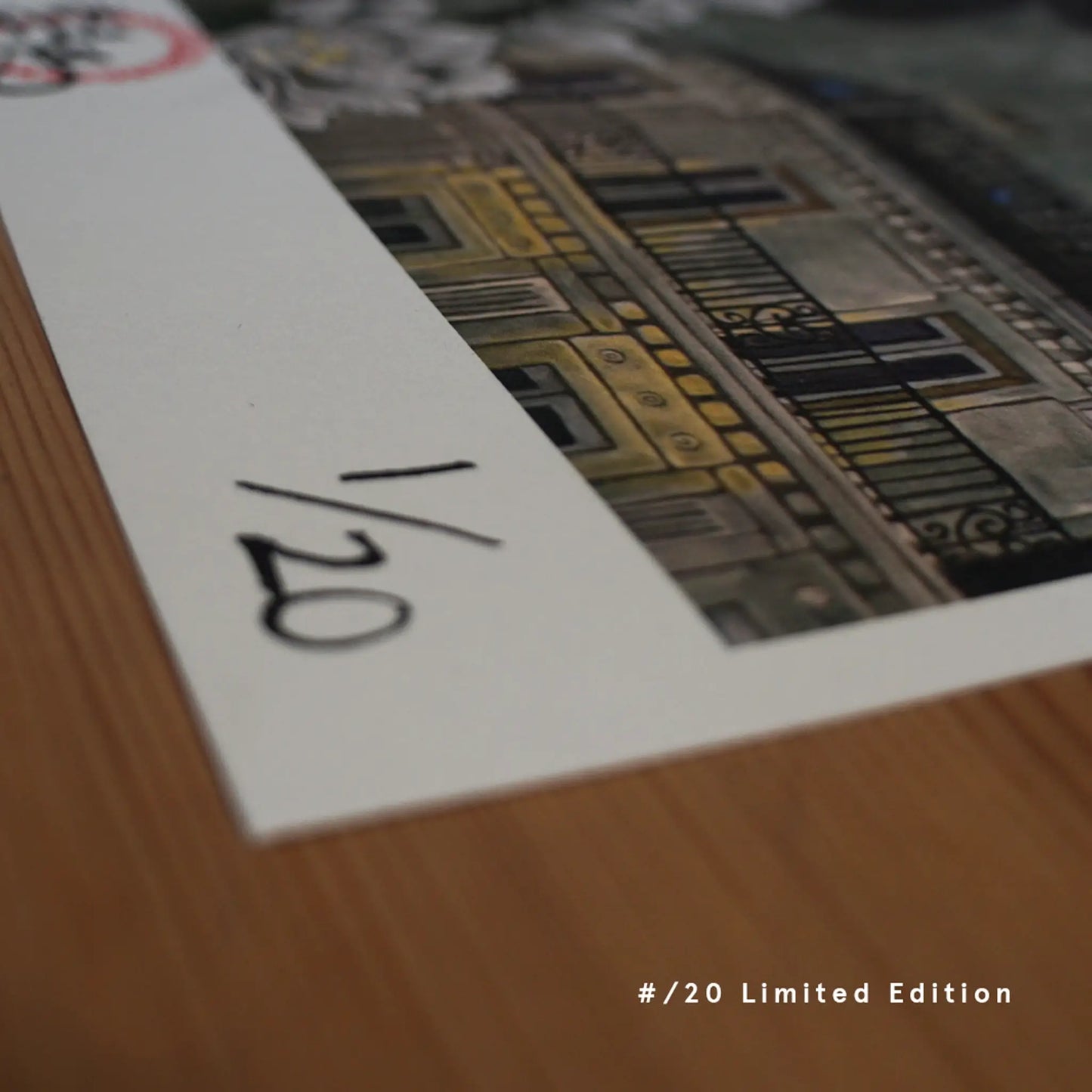 A close-up of a hand-numbered "1/20" limited edition fine art print by Ryuku Otsuka. Resting on a warm wooden table, the print showcases the edge of a detailed painting featuring a classic architectural facade with balconies, offering a quiet, premium sanctuary for collectors.