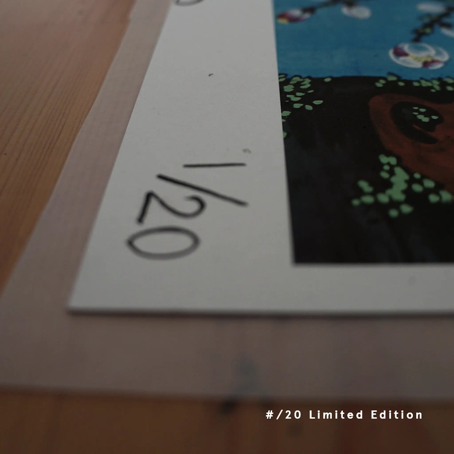 A close-up of a hand-numbered "1/20" limited-edition fine art print of "pride" by Ryuku Otsuka. Resting on a warm wooden surface, the print edge showcases delicate white plum blossoms against a deep blue background, representing a calm, intentional sanctuary of traditional craftsmanship.