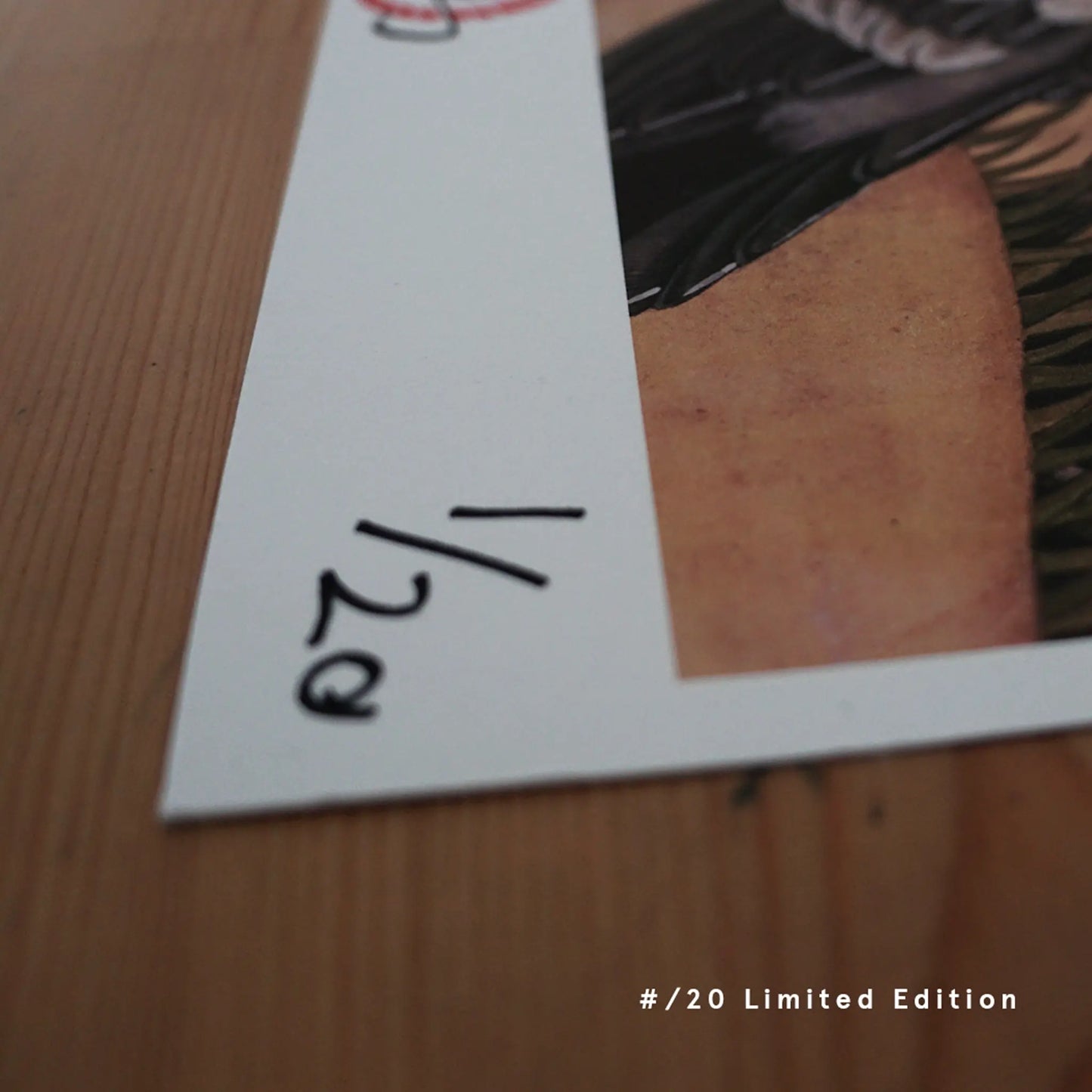 A close-up photograph showing the lower corner of a heavy-weight fine art print by Ryuku Otsuka, resting on a wooden surface. The white margin clearly displays a hand-written edition number "1/20" in black ink, alongside a red hanko seal impression, highlighting the limited run of 20 prints, authenticity, and artisan craftsmanship.