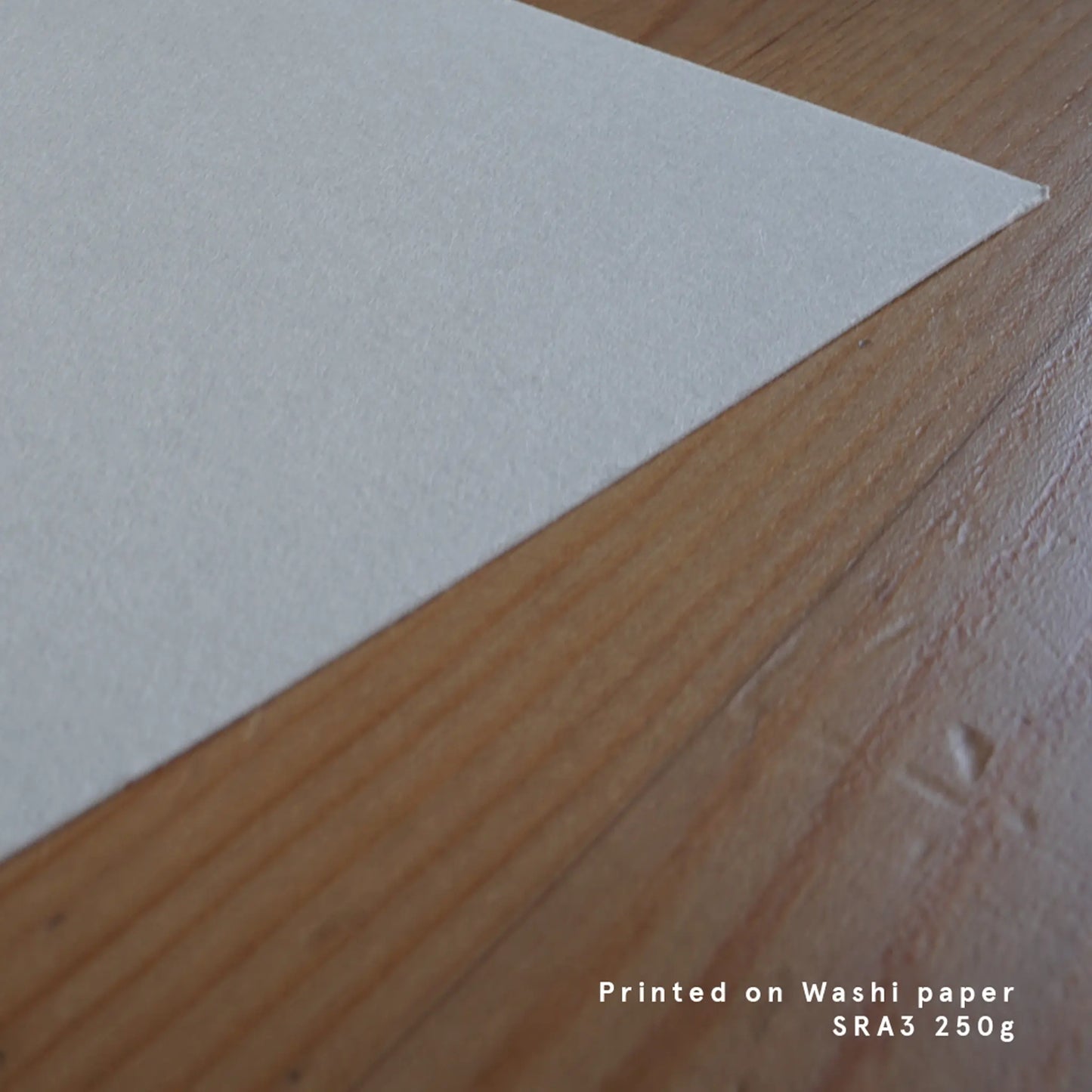 A close-up detail shot showcasing the natural, fibrous texture of premium SRA3 250g Japanese Washi paper on a warm wooden surface. The shot highlights the organic and tactile quality of the paper used for Ryuku Otsuka's limited-edition Nihonga prints, offering a visual sense of calm, slow-crafted patience, and quiet luxury.