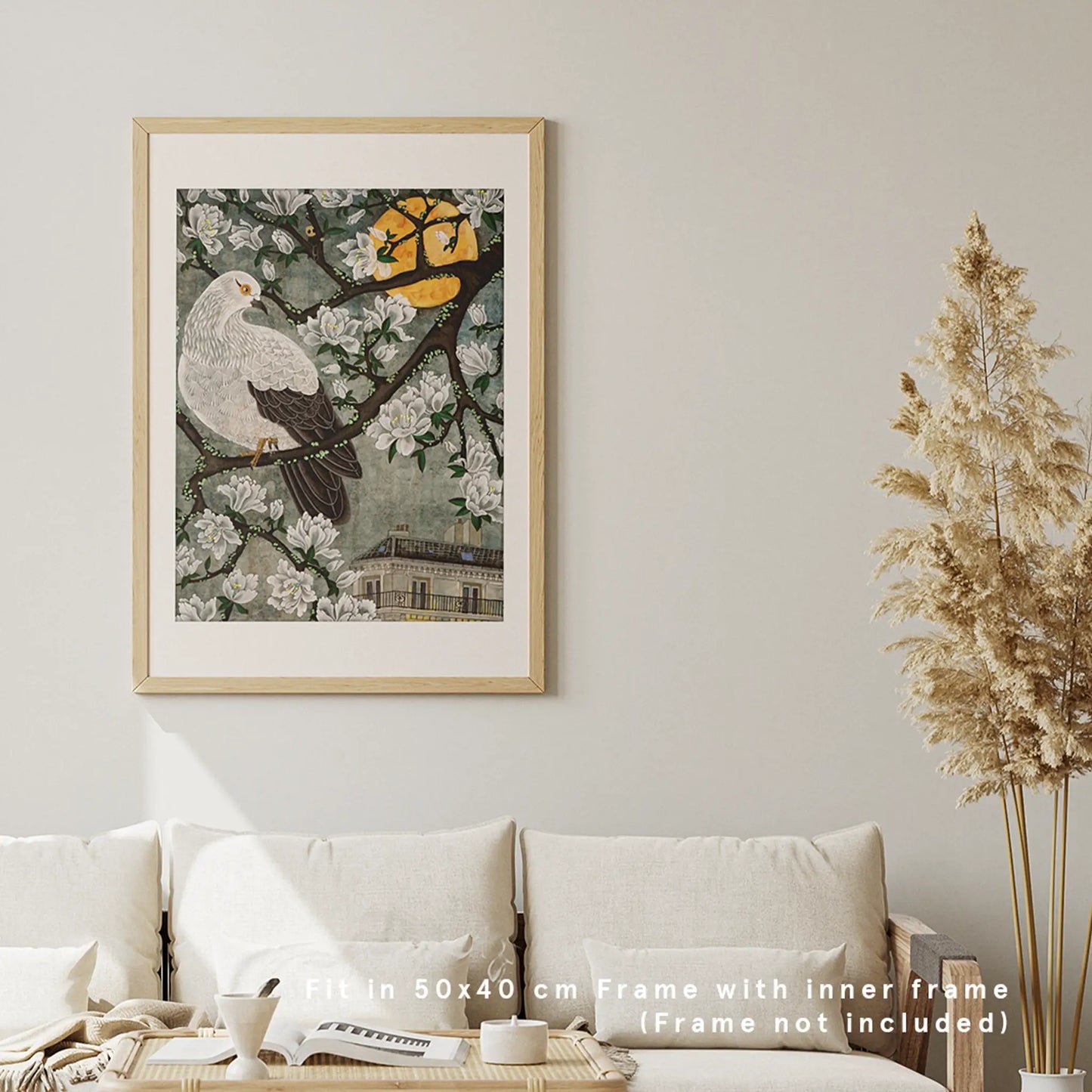 A framed 50x40 cm "Dream" kacho print with a white pigeon, full moon, and Parisian facade hanging on a neutral wall above a cream living room sofa.