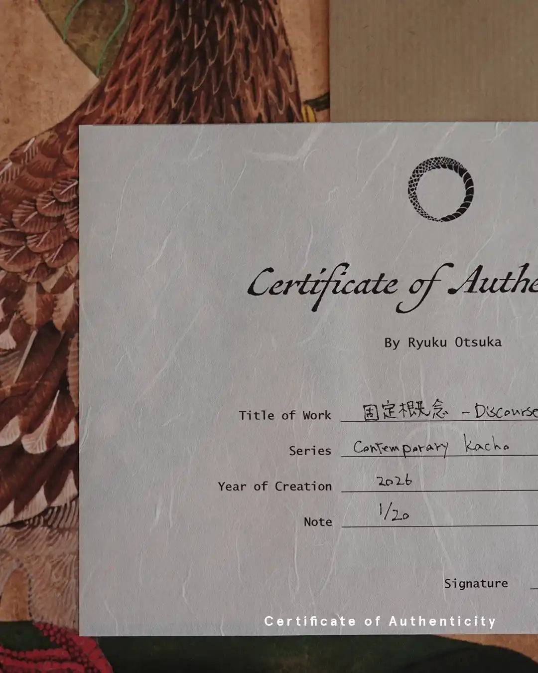 A close-up photograph of a Certificate of Authenticity printed on textured white washi paper for the fine art print "固定概念 - Discourse -" by Ryuku Otsuka. The document details the series "Contemporary kacho," creation year 2026, and edition number "1/20," set against a background of intricate brown feather artwork.