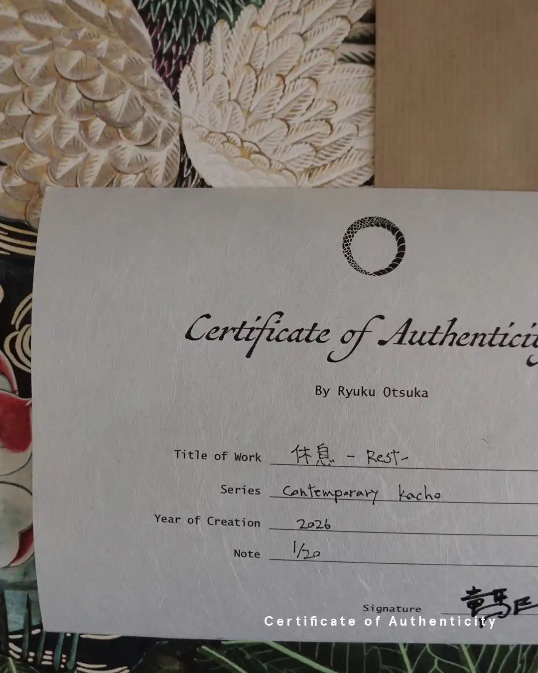 A close-up photograph of a Certificate of Authenticity printed on textured white washi paper for the fine art print "休息 - Rest -" by Ryuku Otsuka. The document details the series "Contemporary kacho," creation year 2026, limited edition number "1/20," and the artist's signature in Japanese kanji at the bottom right, set against a background of detailed white feather artwork.