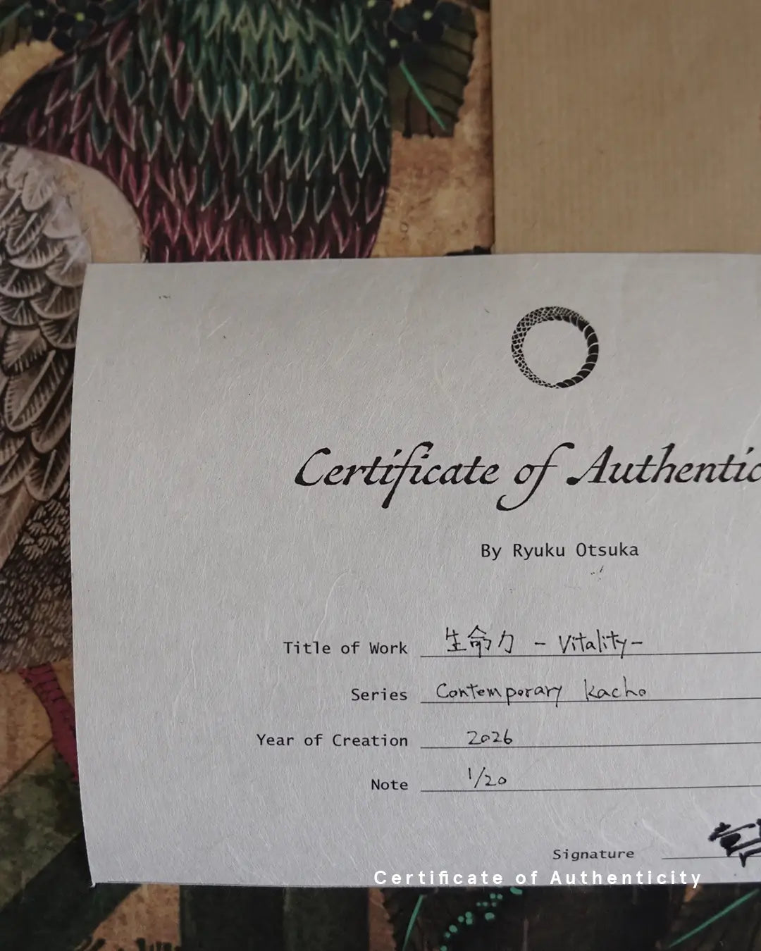 A close-up photograph of a Certificate of Authenticity printed on textured white washi paper for the fine art print "生命力 - Vitality -" by Ryuku Otsuka. The document lists the series "Contemporary kacho," creation year 2026, limited edition numbering "1/20," and the artist's signature in Japanese kanji at the bottom right, set against a backdrop of detailed feather patterns from a pigeon artwork.