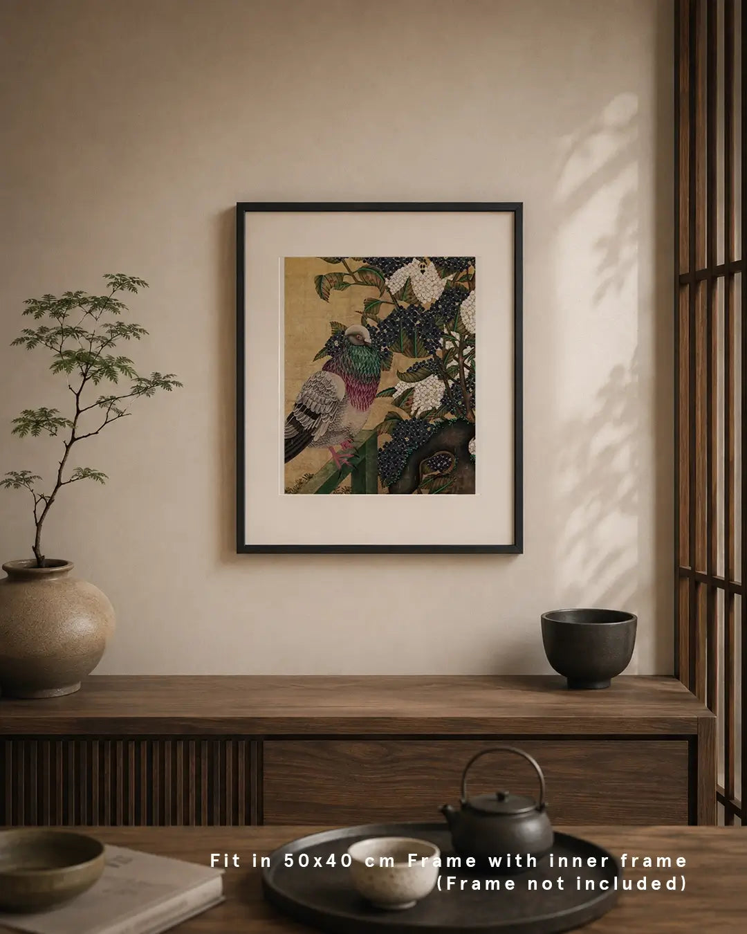 An interior mockup featuring a framed Japanese Nihonga art print on a light beige wall above a dark wooden sideboard. The artwork depicts an urban pigeon perched among hydrangea blossoms against a shimmering gold leaf background. The warm, minimalist room setup includes a potted bonsai tree, a ceramic bowl, and a Japanese teaset on a tray, with text at the bottom reading "Fit in 50x40 cm Frame with inner frame (Frame not included)."