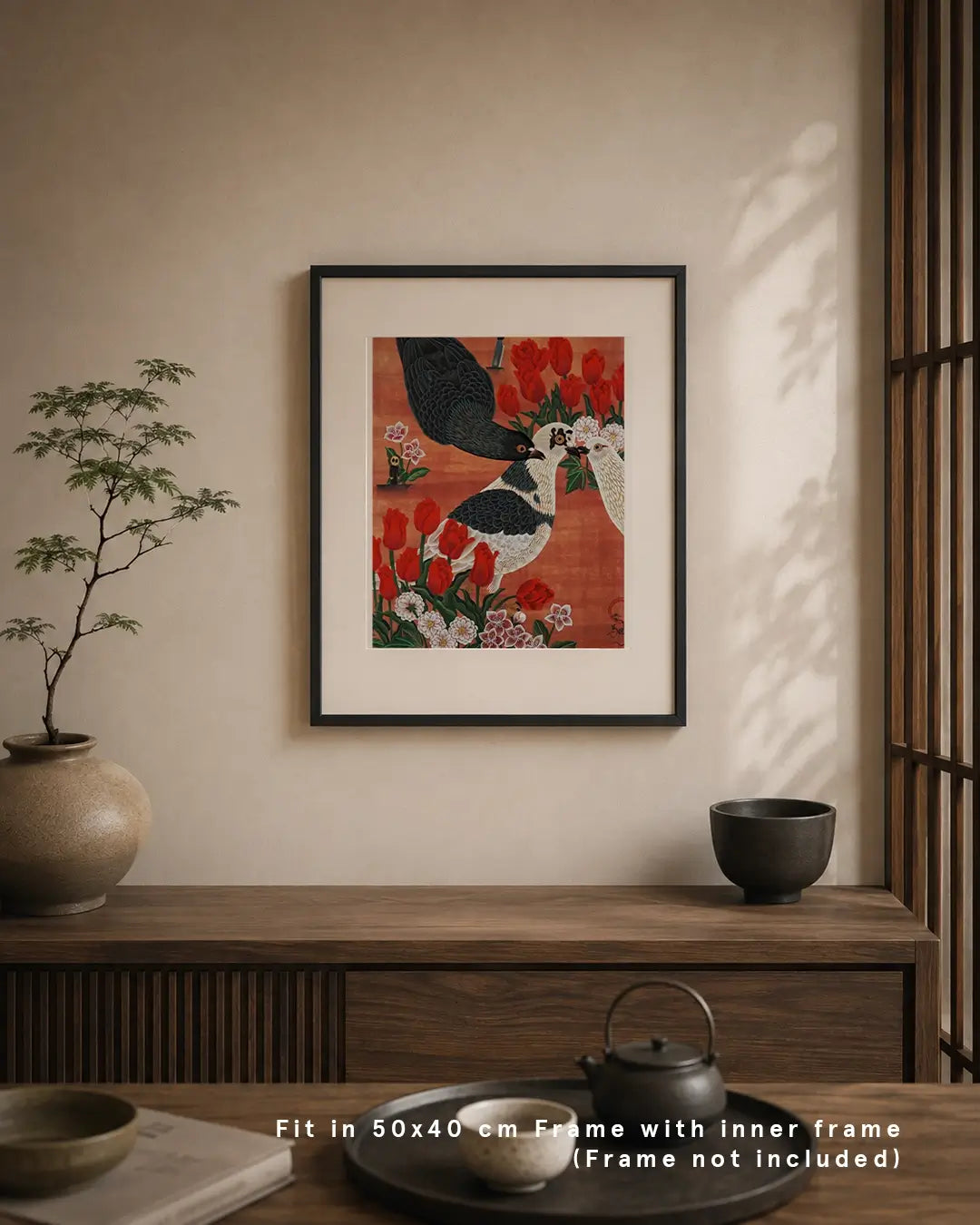 An interior mockup featuring a framed Japanese Nihonga art print hanging on a warm beige wall above a dark wood console table. The artwork depicts urban pigeons surrounded by red tulips, plum blossoms, and small flowers against a rich reddish-brown backdrop. The minimalist room setting includes a bonsai-style potted plant, ceramic bowl, and a teaset on a tray, with text overlay at the bottom reading "Fit in 50x40 cm Frame with inner frame (Frame not included)."