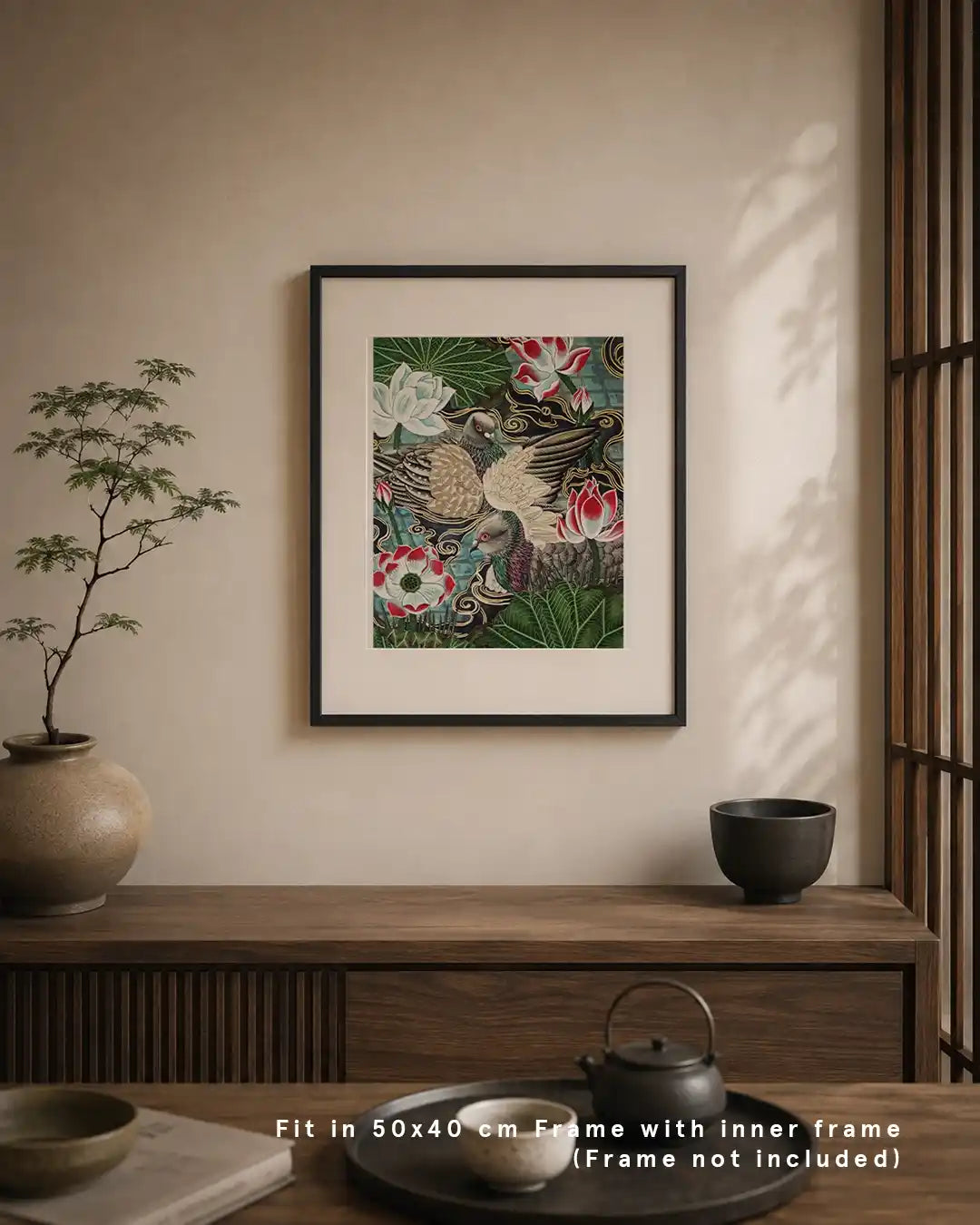 A framed Japanese Nihonga art print displayed on a warm beige wall above a dark wooden credenza. The artwork depicts two urban pigeons surrounded by vibrant red and white water lily blossoms and dark green leaves. The modern interior room setting features a potted plant, a ceramic teaset, and text overlay reading "Fit in 50x40 cm Frame with inner frame (Frame not included)."