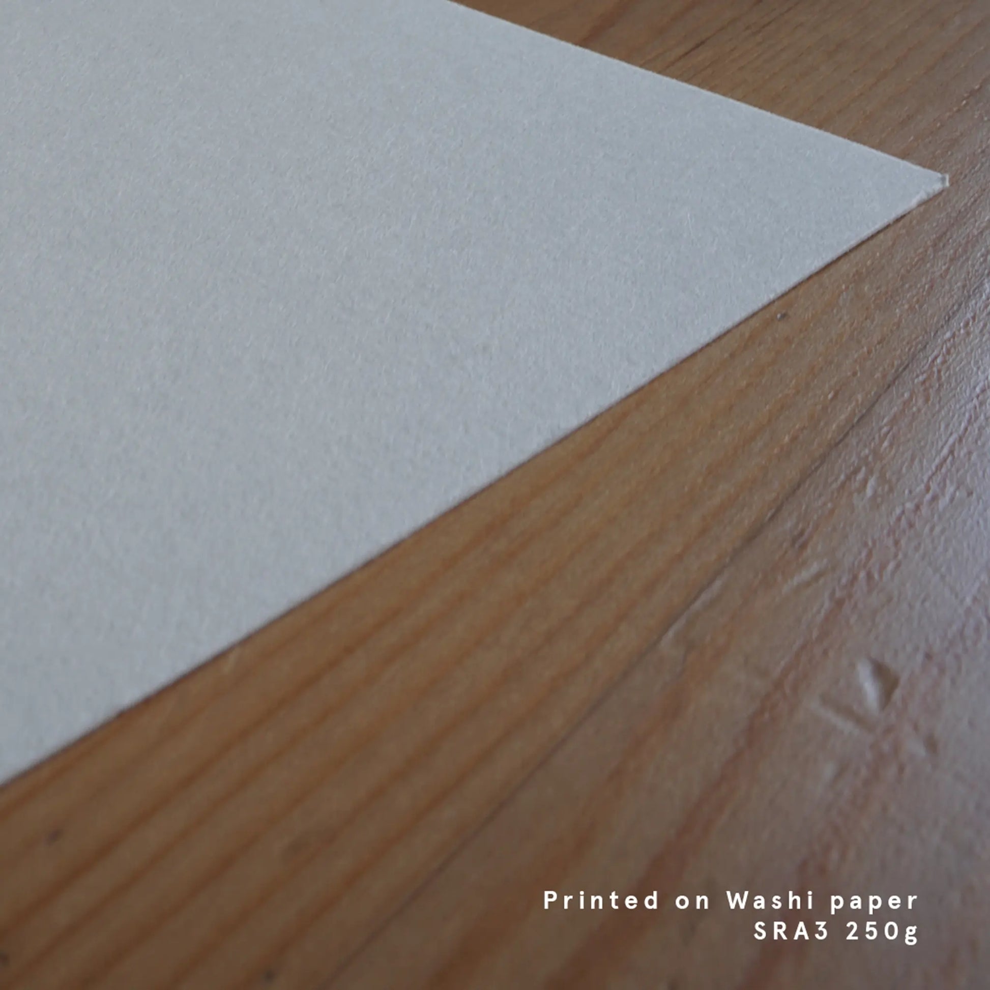 Close-up shot of a thick, textured white Washi paper corner resting on a wooden surface, highlighting the premium quality of the fine art print.